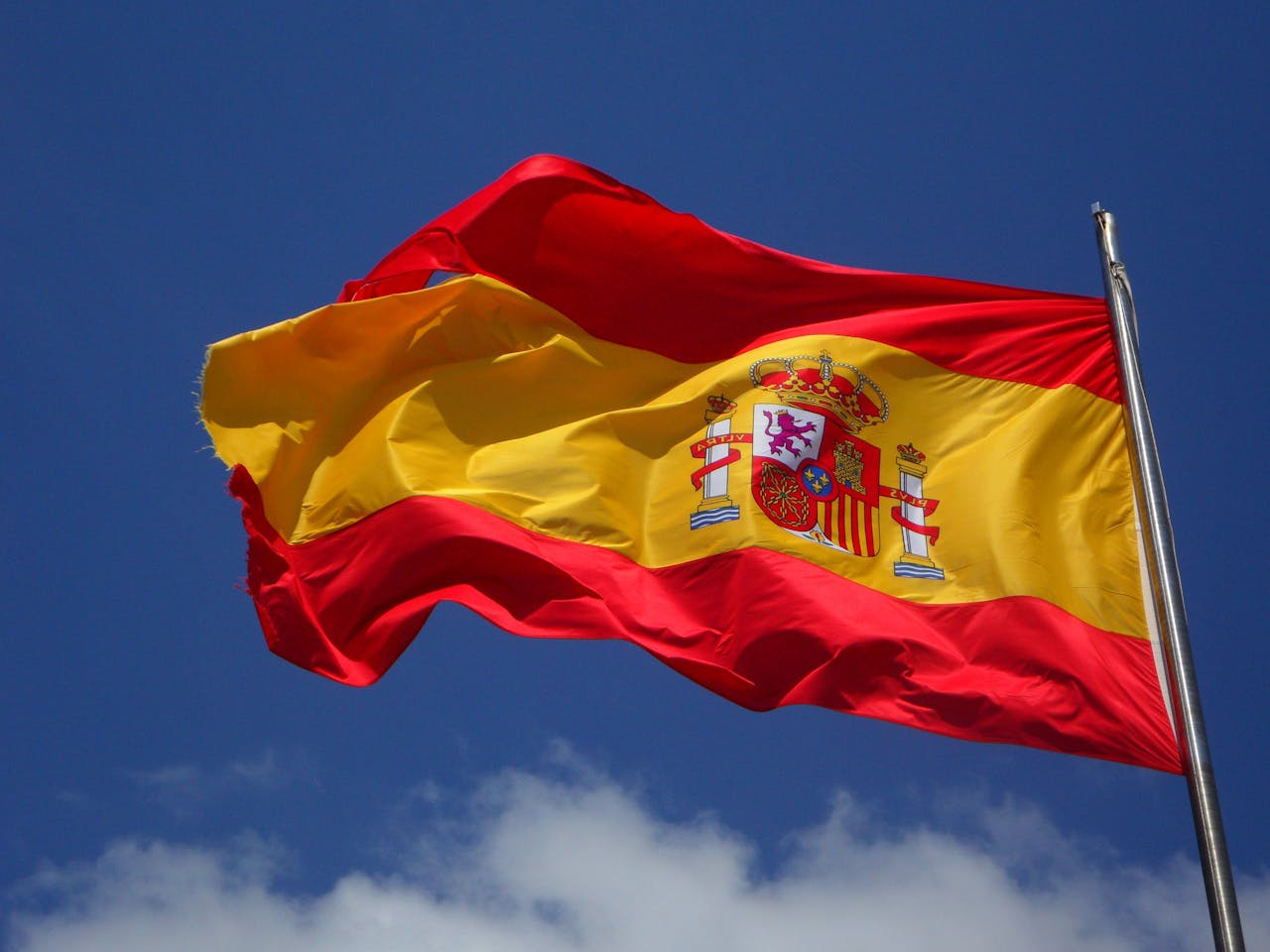 why-choose-me Vibrant Spanish flag waving against a clear blue sky and clouds.